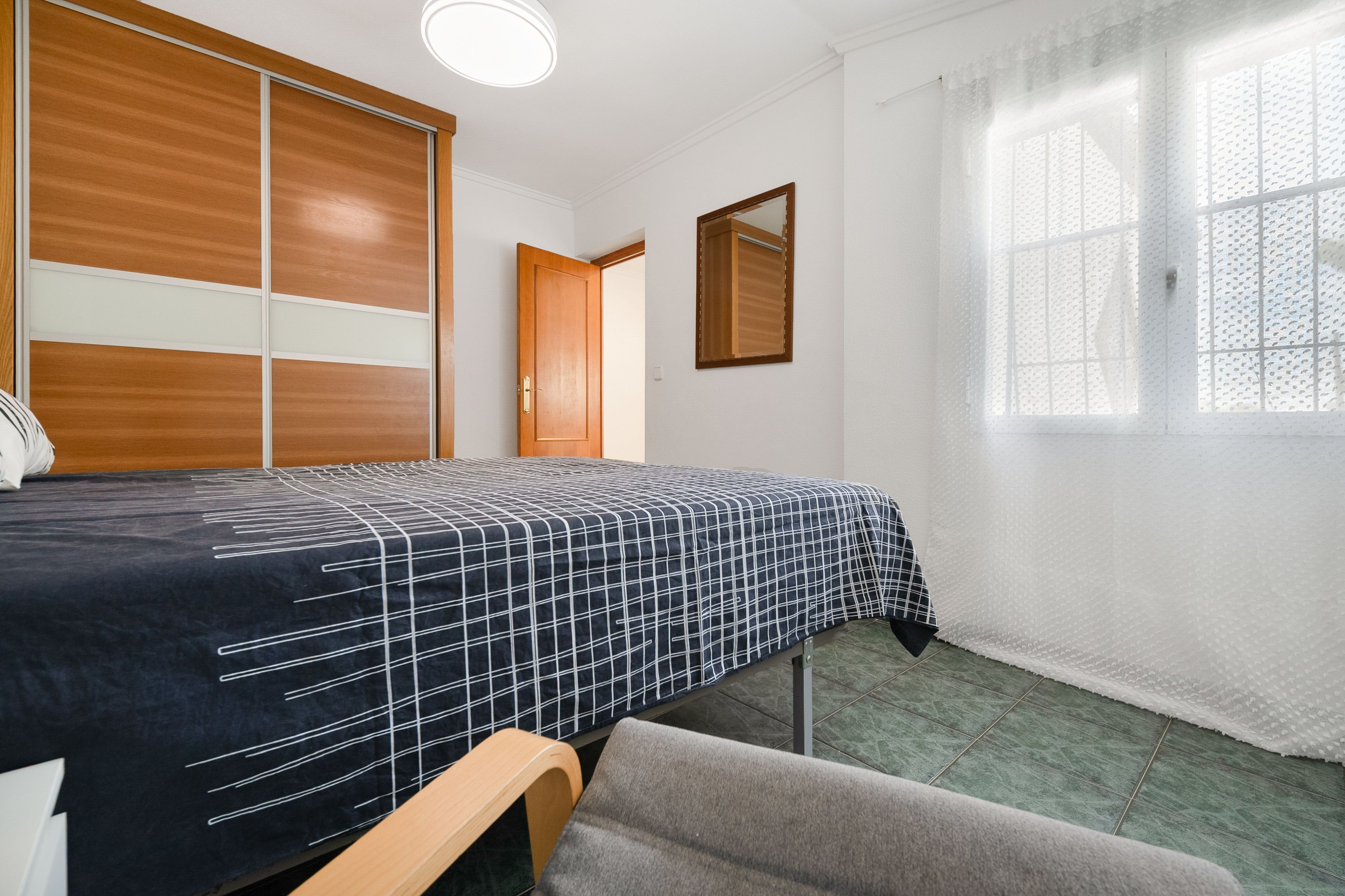 Un dormitorio con una cama, un armario de madera, una ventana con cortina y una puerta.