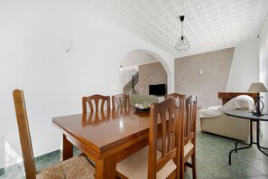 A dining area with a wooden table and chairs, a sofa, and a TV in the background.