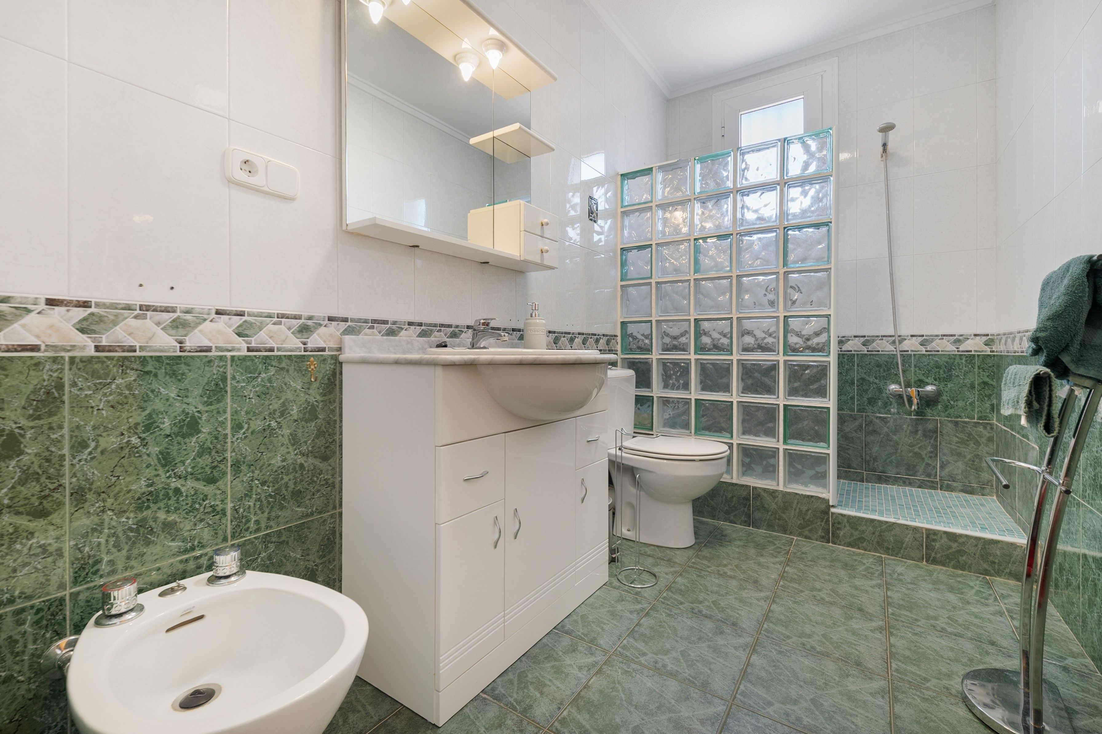A bathroom with a bidet, toilet, and a glass shower enclosure.