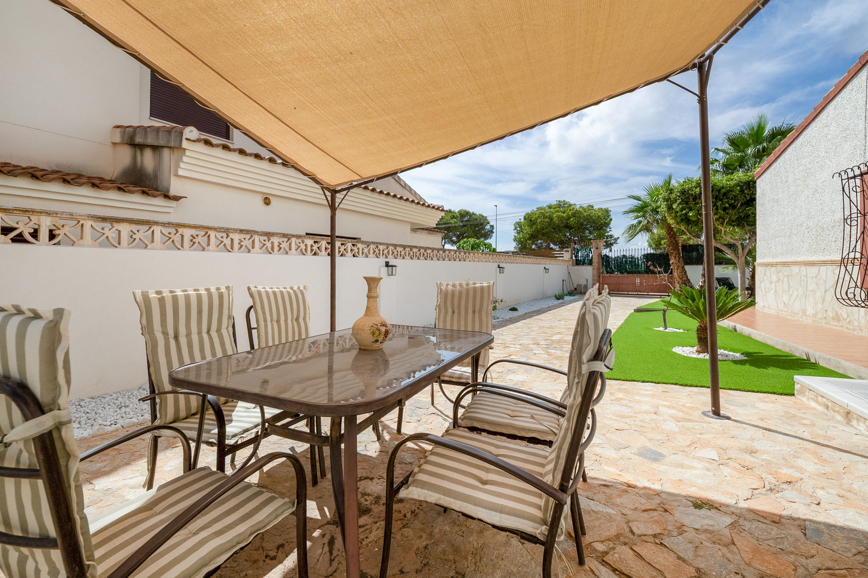 Eine Terrasse im Freien mit Tisch und Stühlen, einer Zierflasche und einer Pergola, die Schatten spendet.