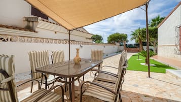An outdoor patio with a table and chairs, a decorative vase, and a pergola providing shade.