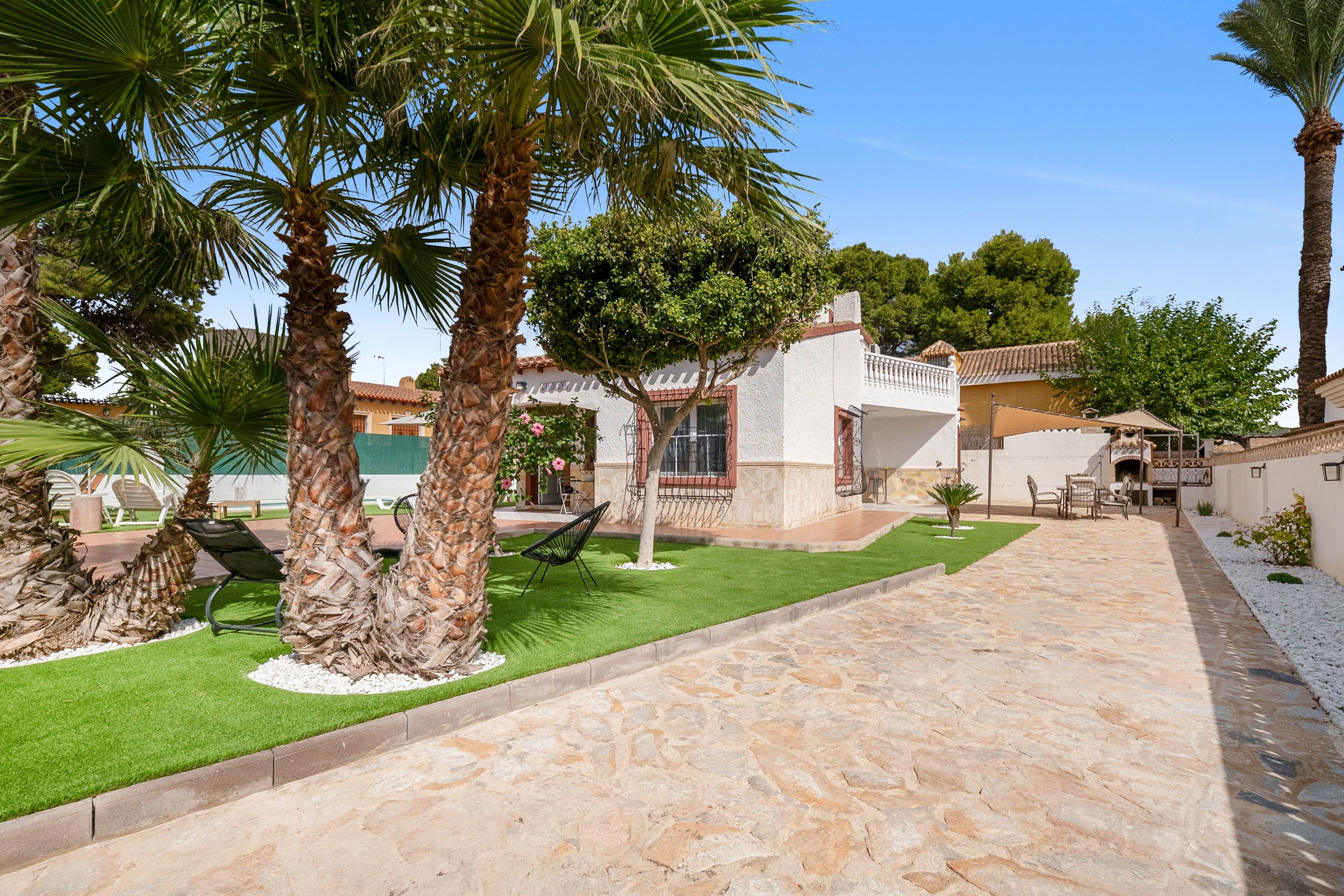 Un patio con palmeras, un sendero de piedra y un edificio blanco con balcón.