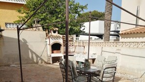 Un patio esterno con pavimento in pietra, un tavolo con sedie e un barbecue.