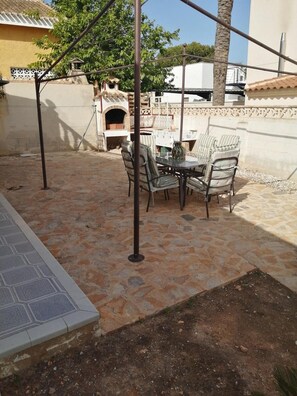 An outdoor patio with a stone floor, a table with chairs, and a grill.
