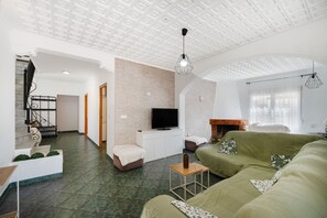 A spacious living room with a green sofa, a flat-screen TV, and a fireplace.