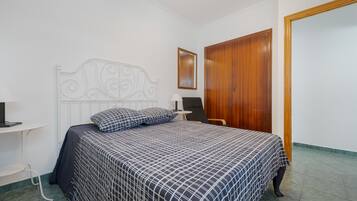 A bedroom with a bed, a wooden wardrobe, a bedside table, and a mirror on the wall.