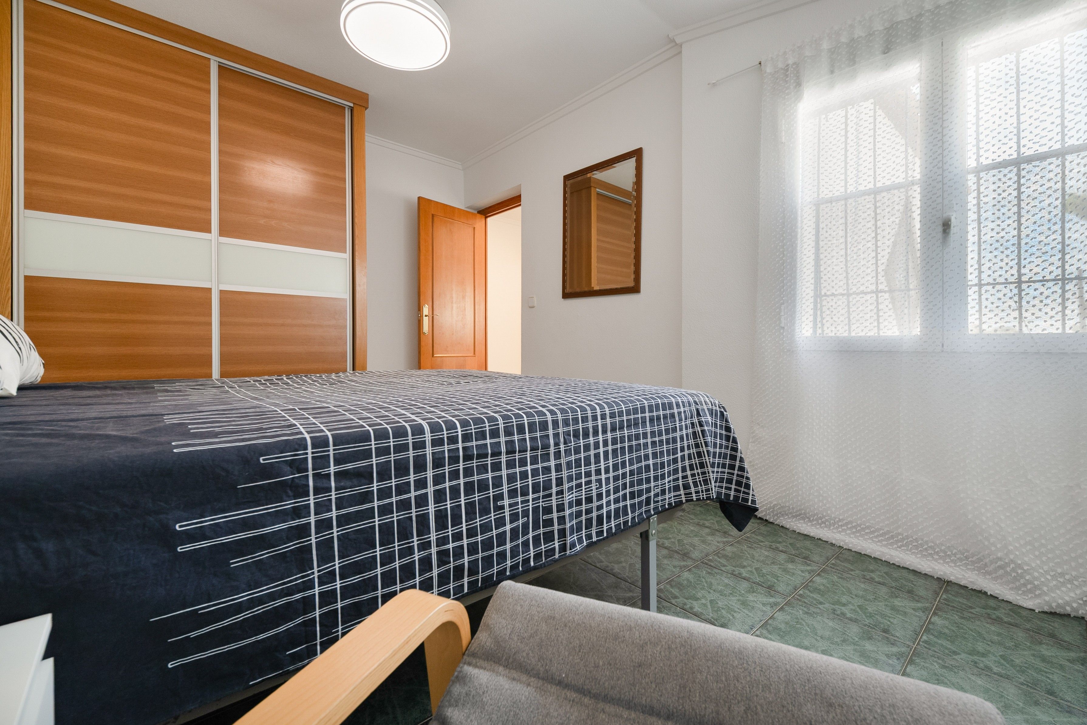Een slaapkamer met een bed, een kledingkast, een raam met gordijnen en een deur.