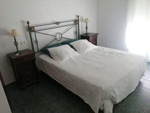 A neatly made bed with white linens, a green headboard, and two bedside tables with lamps.