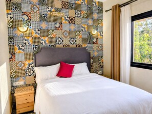 A hotel room with a bed, a nightstand, a wooden dresser, and a patterned wall. - Luxurious 5-bedroom house in quaint Sidi Kaouki  150m walk from the beach (Sidi Kaouki)
