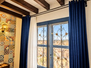 Ein Zimmer mit einer Wand aus gemusterten Fliesen, einem Fenster mit verzierten Metallgitter und Blick auf eine Landschaft.