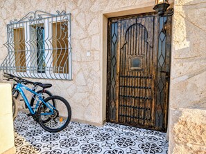 Ein blaues Fahrrad steht neben einer Steinmauer mit einem schmiedeeisernen Tor und einem Kachelboden.