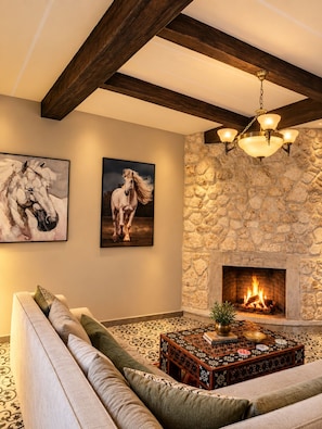 A living room with a stone fireplace, a sofa, a coffee table with decorative items, and two horse paintings on the wall. - Luxurious 5-bedroom house in quaint Sidi Kaouki  150m walk from the beach (Sidi Kaouki)