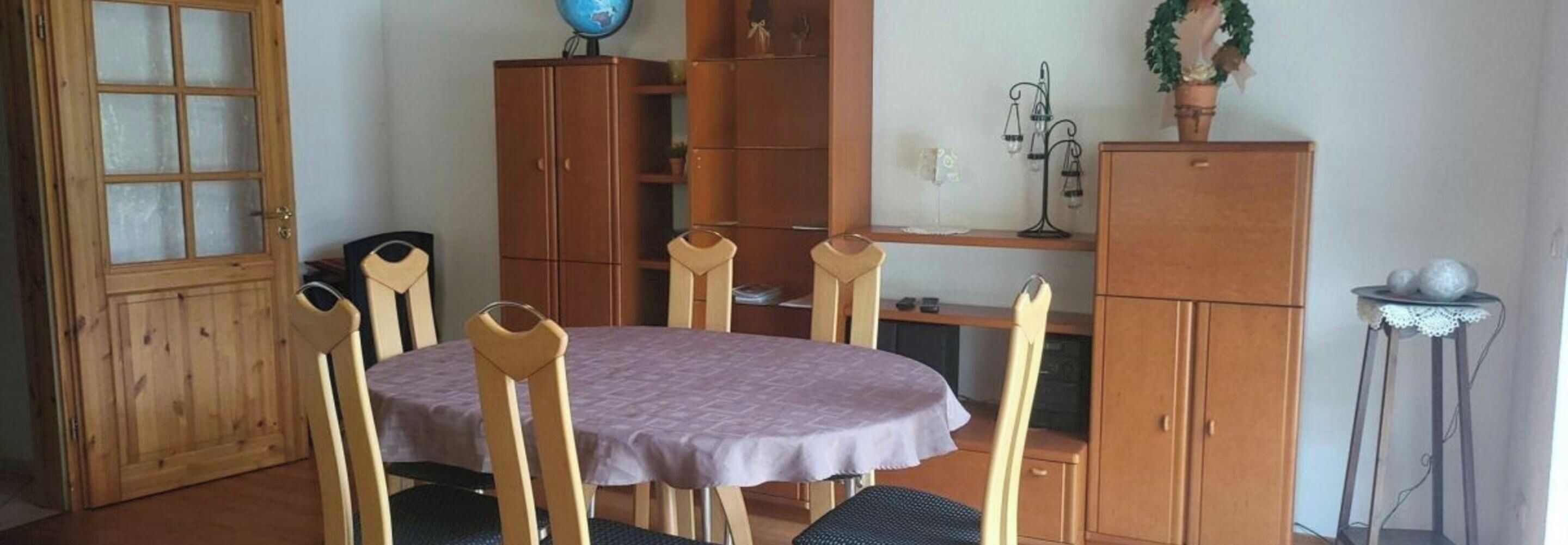 Un comedor con una mesa redonda, sillas de madera, un armario y un globo terráqueo en una estantería.