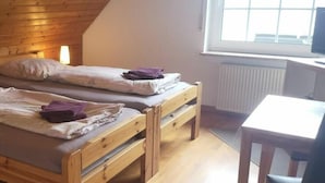 A room with two wooden beds, each with a pillow and a folded towel. There is a small table and a chair to the right, and a window providing natural light. - Holiday Apartment in Eggstedt With Terrace (Eggstedt)