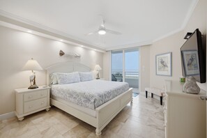 Une chambre à coucher avec un lit, des tables de chevet, un ventilateur de plafond et des œuvres d’art accrochées aux murs.