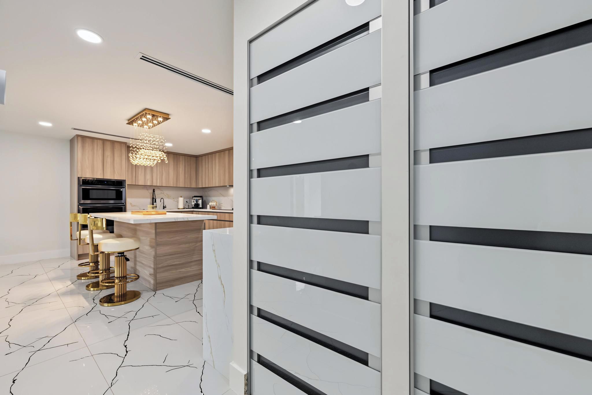 A modern kitchen with a marble floor, a central island, and a bar area with stools.