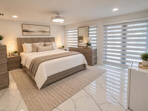 A modern bedroom with a large bed, bedside tables, a nightstand, a mirror, and a window with blinds. - Modern Waterfront Retreat Oversize outdoor Tiki, kitchen and heated SPA (Fort Lauderdale)