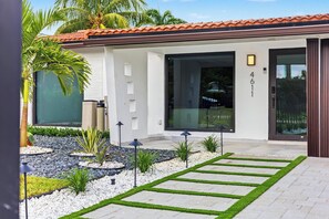 A modern house with a tiled roof, large windows, and a well-maintained garden with a stone pathway. - Modern Waterfront Retreat Oversize outdoor Tiki, kitchen and heated SPA (Fort Lauderdale)