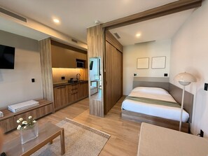 Ein modernes Hotelzimmer mit Küchenzeile, einem Bett, einem Nachttisch und einer Lampe.