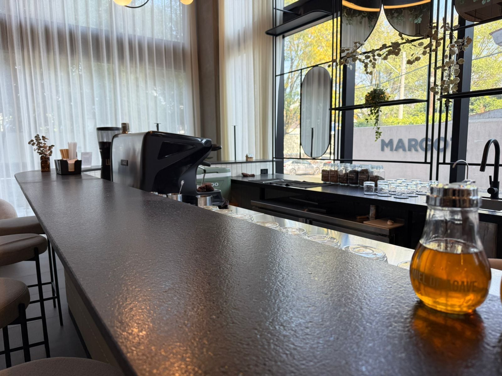 A modern kitchen with a bar area, a coffee machine, and a view of the street outside.