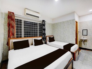 A hotel room with two beds, an air conditioning unit, a window with a grid pattern, a bathroom with a sink and mirror, and a marble wall. - Super Hotel O Porur Jeya's Elite (Chennai)