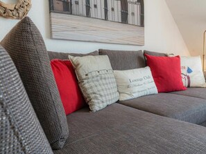A grey sofa with multiple cushions, including a red one and a white pillow with text. - Holiday Apartment 4 "muller" (St. Peter-Ording)