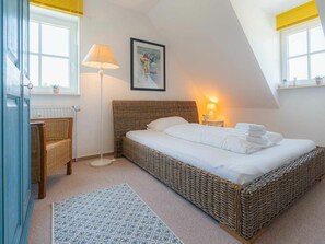 A bedroom with a bed, a chair, a floor lamp, a painting, and a window with curtains. - Holiday Apartment 4 "muller" (St. Peter-Ording)