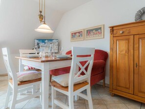 A dining area with a wooden table, white chairs, and a red sofa. There is a wooden cabinet to the right. - Holiday Apartment 4 "muller" (St. Peter-Ording)