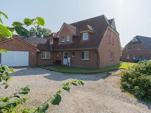A two-story house with a garage, a front porch, and a gravel driveway. - Holiday Apartment 4 "muller" (St. Peter-Ording)