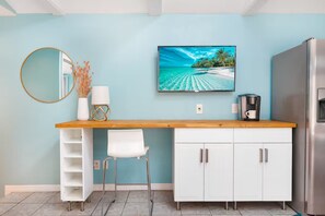 A kitchen with a wooden countertop, white cabinets, a white chair, a round mirror, a wall-mounted TV, and a refrigerator. - Private Guesthouse Near Beach & Downtown (St. Petersburg)