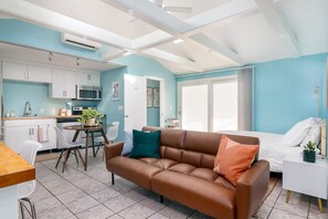 A modern kitchen with white cabinets, a microwave, and a dining area with a brown leather sofa and a white table. - Private Guesthouse Near Beach & Downtown (St. Petersburg)