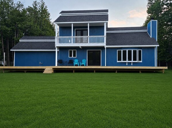 Une maison à deux étages avec un balcon, une terrasse et une cour gazonnée.