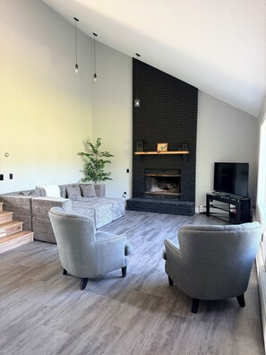 Ein modernes Wohnzimmer mit Kamin, grauen Sofas und einem Fernseher.