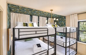 A room with bunk beds, a patterned wall, a chandelier, and a window with curtains. - Pool, Hot Tub, Sauna, 11 Beds, Rooftop Kitchen (Nashville)