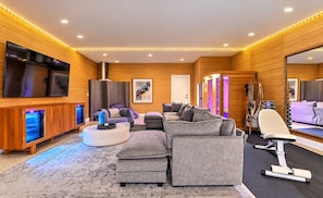A modern living room with a large flat-screen TV, grey sofas, a massage chair, and a wooden wall with built-in lighting. - Pool, Hot Tub, Sauna, 11 Beds, Rooftop Kitchen (Nashville)