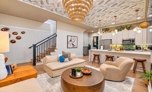 A modern living room with a sofa, coffee table, and a staircase leading to an upper level. - Pool, Hot Tub, Sauna, 11 Beds, Rooftop Kitchen (Nashville)