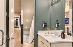 A modern bathroom with a large mirror, two towel hooks, a sink, and a toilet. - Pool, Hot Tub, Sauna, 11 Beds, Rooftop Kitchen (Nashville)