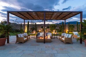 Ein Sitzbereich im Freien mit Korbmöbeln und einer Pergola, mit Blick auf eine Steinmauer und Berge.