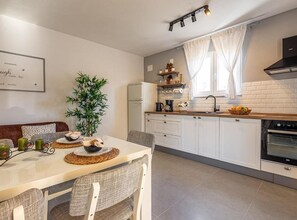 A modern kitchen with white cabinets, a built-in oven, and a dining area with a table set for two. - Three Bedroom Apartment with Balcony (Rogoznica)