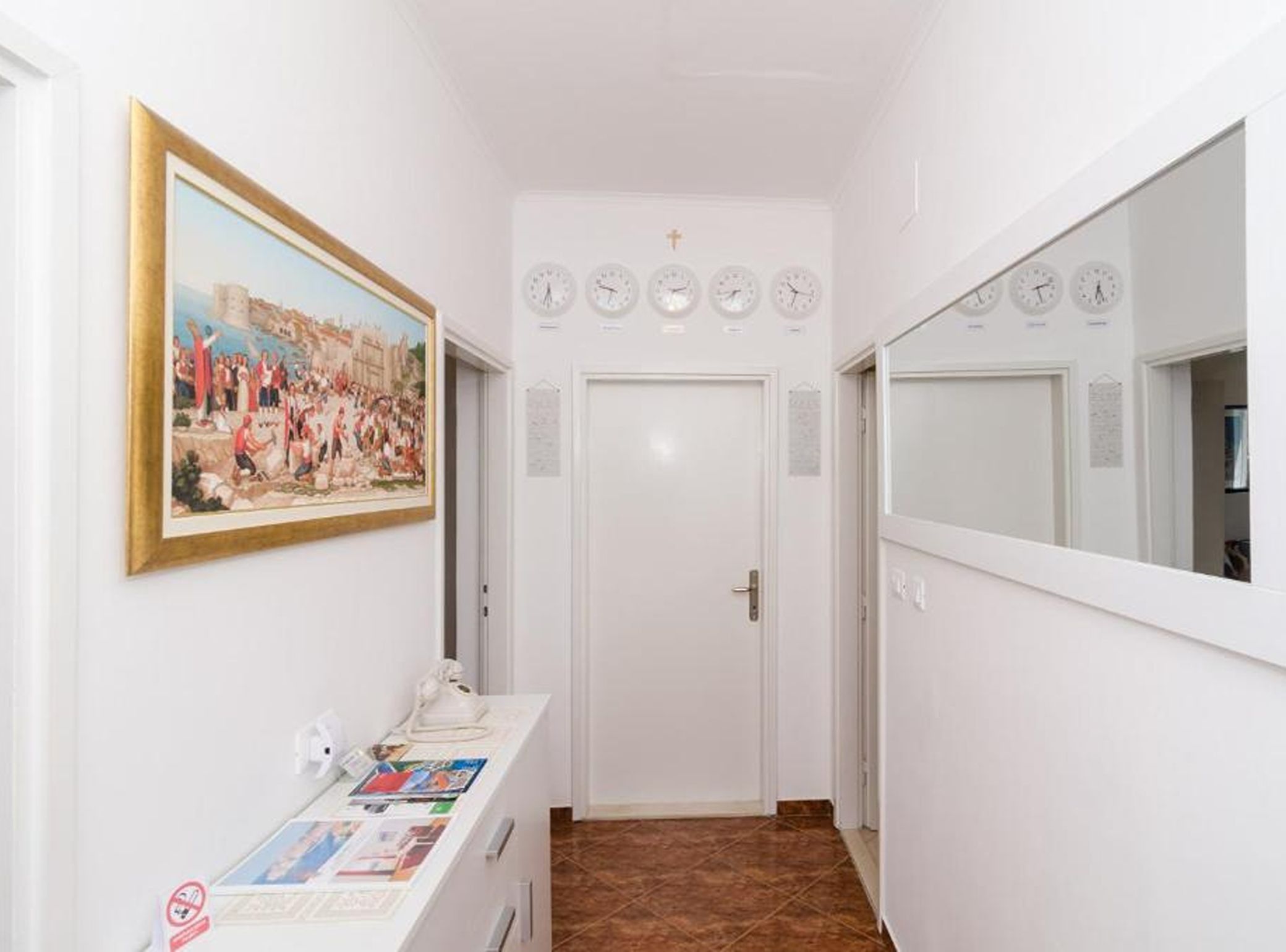 Un couloir avec une porte blanche, un tableau et des horloges au mur.