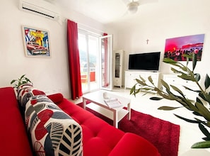 Un salon avec un canapé rouge, une table basse blanche et un téléviseur.