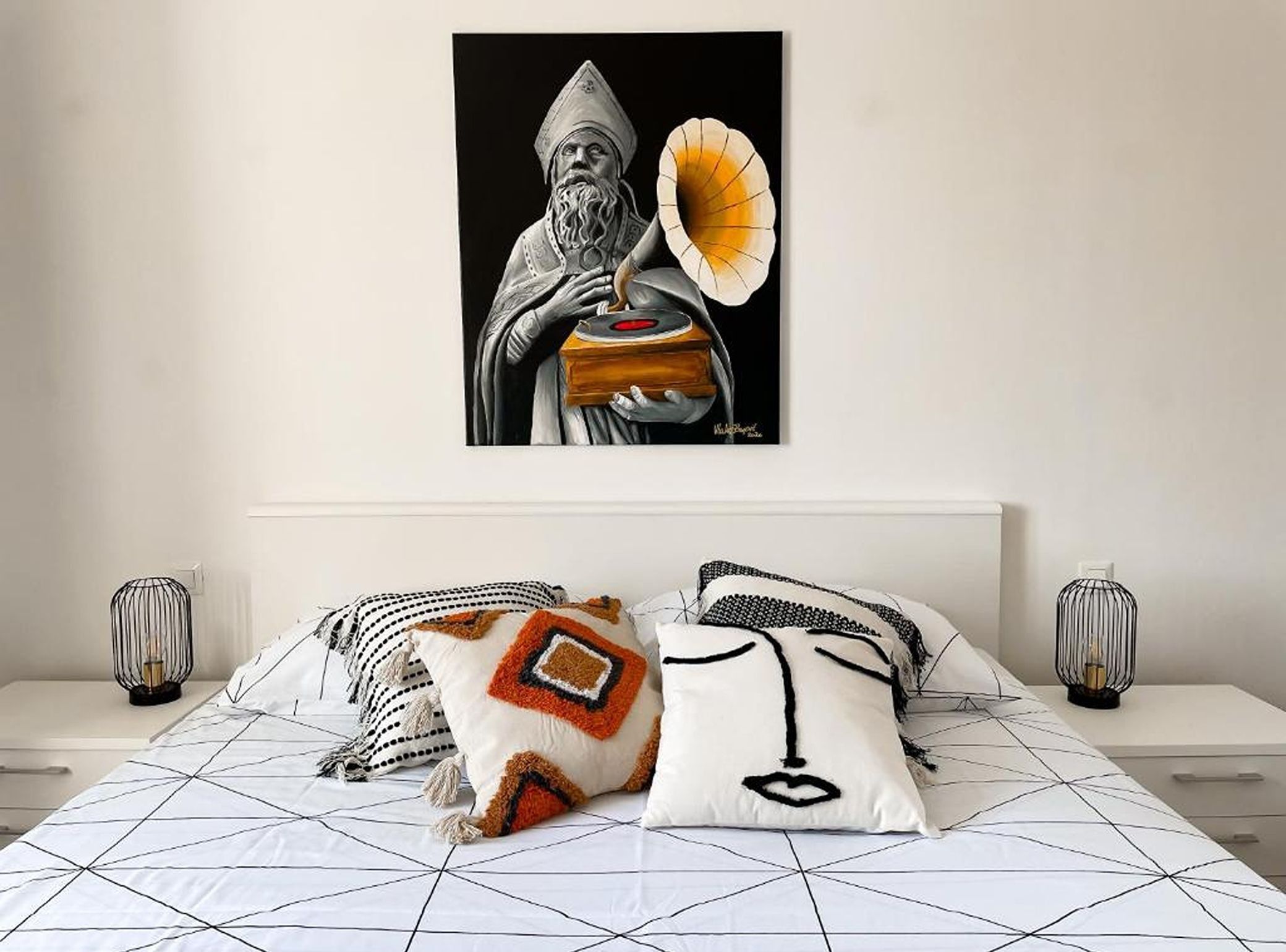 A bedroom with a bed, pillows, a wall-mounted artwork, and bedside lamps.