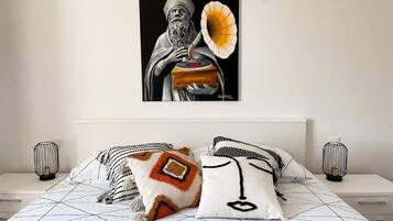 A bedroom with a bed, pillows, a wall-mounted artwork, and bedside lamps.