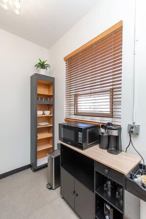 A compact kitchenette with a microwave, coffee maker, and a small shelf unit. - 1BR I Second Story on Main #2, Walk to DT, Queen (Fargo)