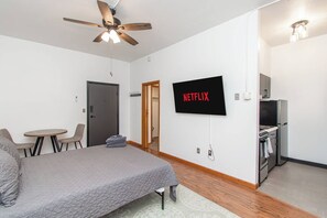 A bedroom with a bed, a TV mounted on the wall, a ceiling fan, and a kitchenette. - 1BR I Second Story on Main #2, Walk to DT, Queen (Fargo)