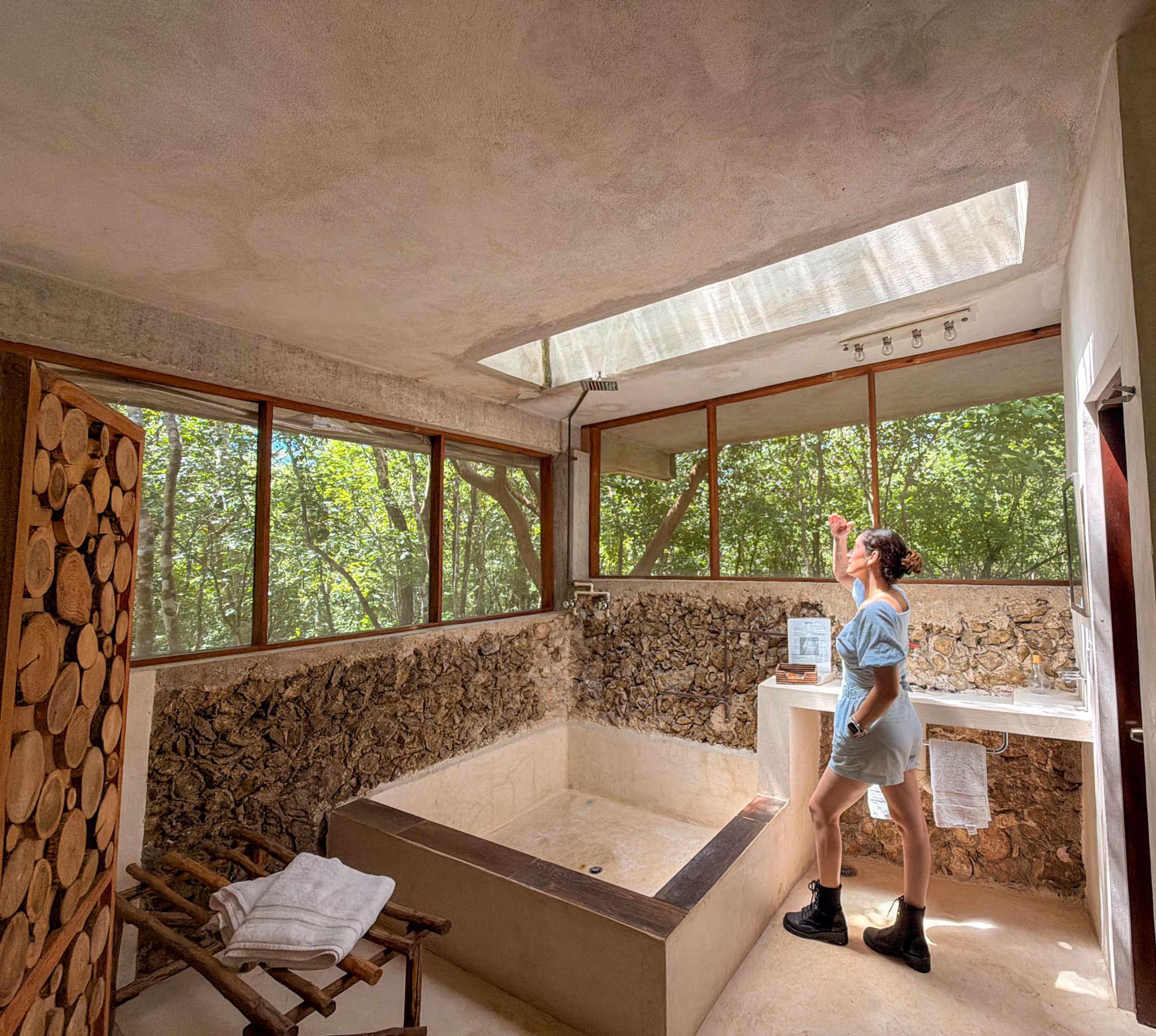 Una habitación con una bañera grande, una pared de troncos de madera y una ventana con vista a árboles.
