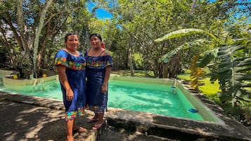 Dos personas junto a una piscina con un jardín tropical al fondo.