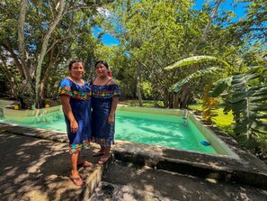 Two individuals standing by a pool with a tropical garden in the background.