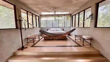 Quarto com cama, rede e escada para uma varanda.