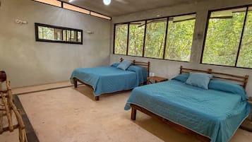 Quarto com duas camas de madeira, um ventilador de teto e janelas com vista para árvores.